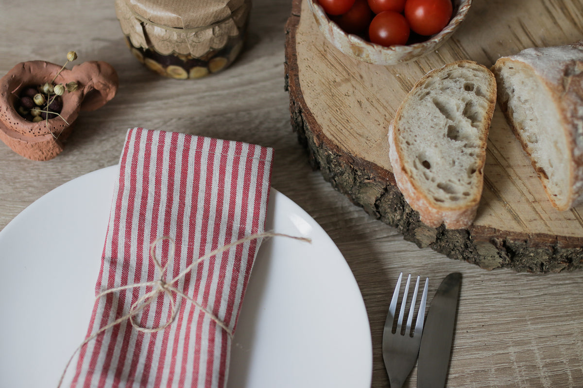 Bread slices on a wooden board with a plate, fork, red white striped linen napkin and knife on a wooden table.