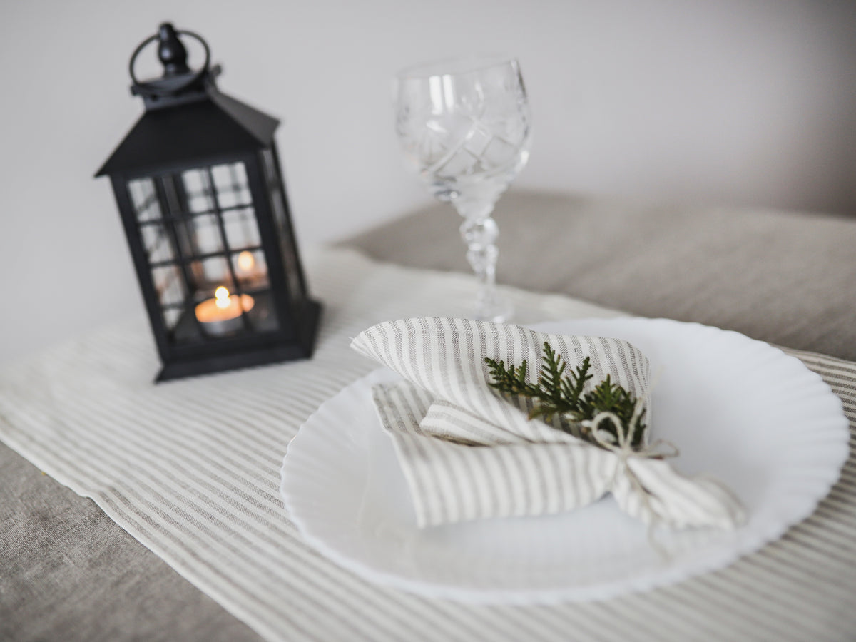 Set table with white plate, striped linen  napkin, and wine glass on a light surface