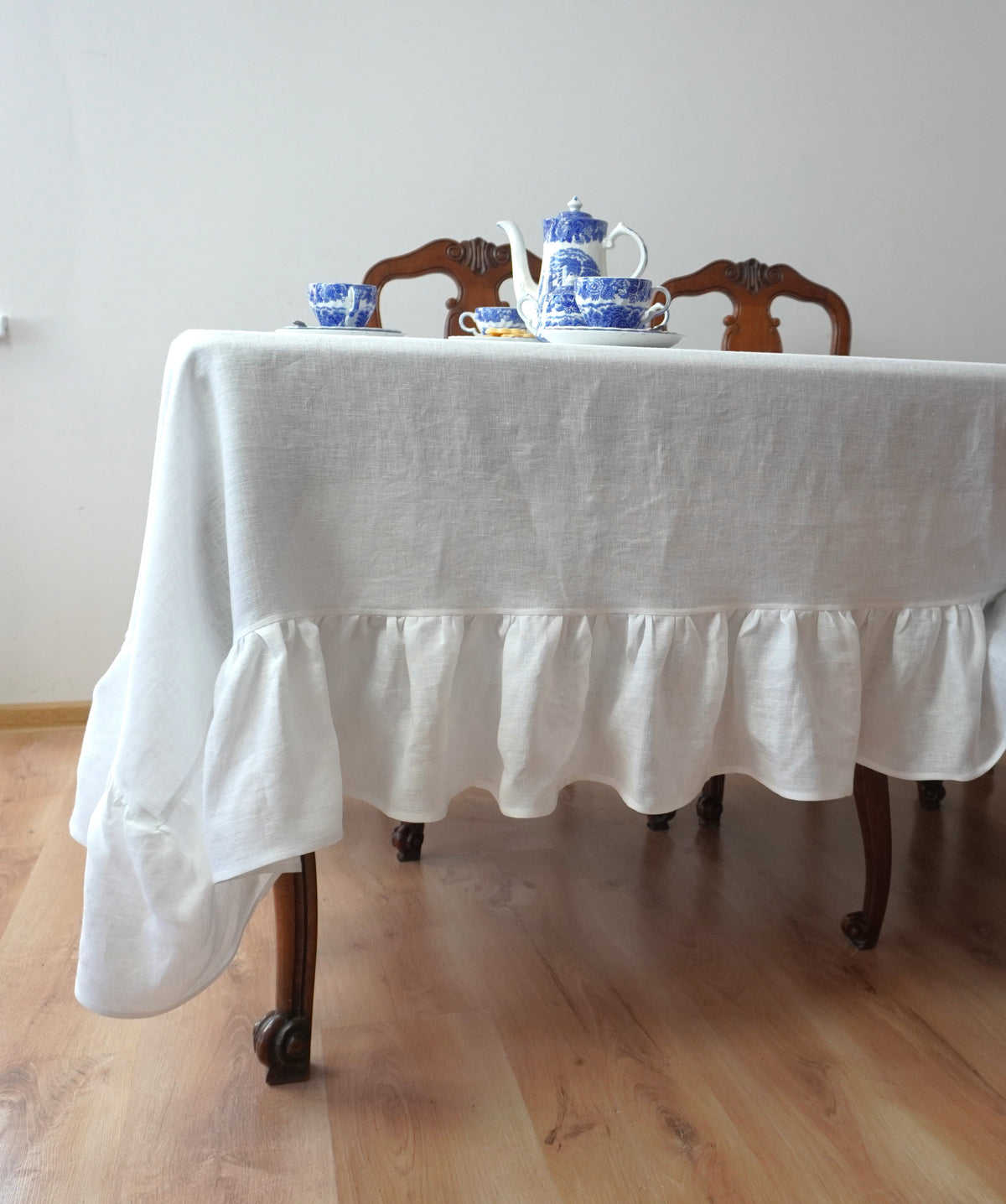 White linen  tablecloth on a wooden table with teacups and a teapot.
