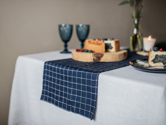 Table setting with a blue checkered runner, cake, and glasses on a neutral background
